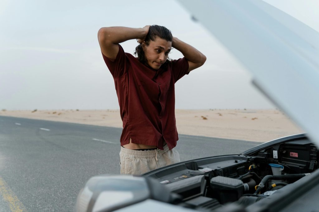 A frustrated man examining a broken car engine in Atlanta, showing stress and concern.